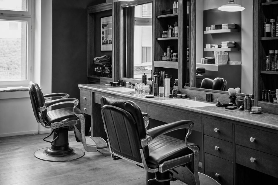 Schwarz-weißes Stimmungsbild: einzelner Frisierstuhl vor großem Spiegel in einem ruhigen Salonraum